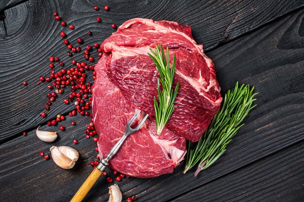 Fresh Raw Chuck eye roll beef steak on butcher table. Black wooden background. Top view.