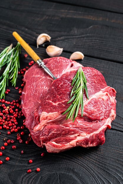 Fresh Raw Chuck eye roll beef steak on butcher table. Black wooden table. Top view.