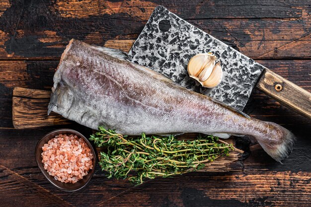 Fresh Raw cod or codfish fish on wooden board with cleaver. Dark Wooden background. Top view.