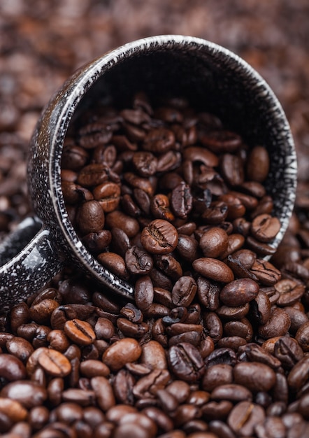 Fresh raw coffee beans in black ceramic cup inside coffee beans background. Macro
