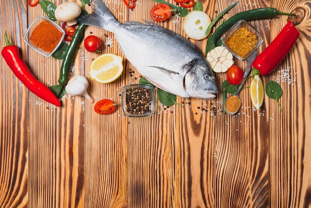 Fresh raw dorado fish on baking paper with lemon, pepper, tomatoes and various spices on wooden surface with copy space.