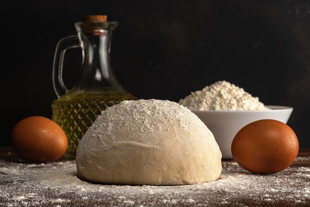 Fresh raw dough for bread or pizza with eggs and oil on a dark wooden table.