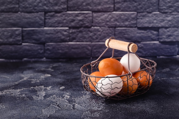 Fresh raw eggs in a metal basket on a dark background