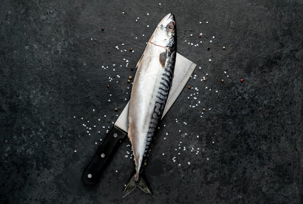 Fresh raw fish mackerel on a knife with spices on a stone background