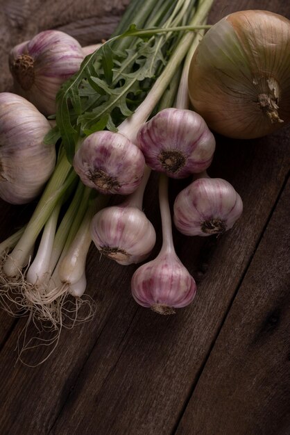 Fresh raw garlic onion and arugula plant on a rustic wooden table Fresh vegetables background