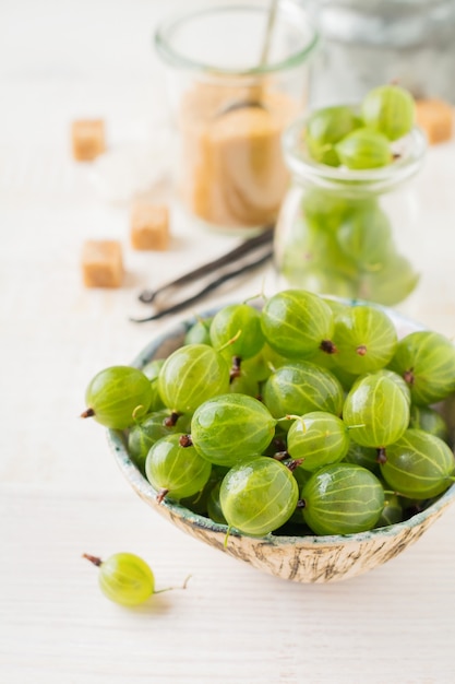 Fresh raw gooseberry berries in white ceramic plate on light wooden.  Rustic style.