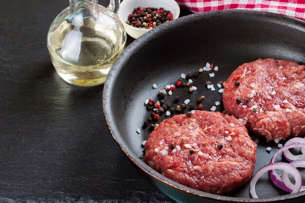 Hamburger di bistecca di manzo macinato fatto in casa crudo fresco con spezie in padella, su un tavolo di ardesia nera, spazio copia, vista dall'alto