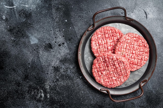 Fresh raw homemade minced beef steak burger in steel tray Black background Top view Copy space