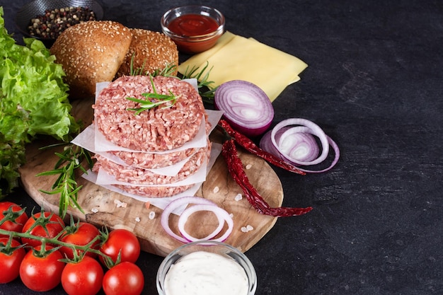 Fresh raw ingredients for homemade burger on black background Unhealthy eating fast food dinner