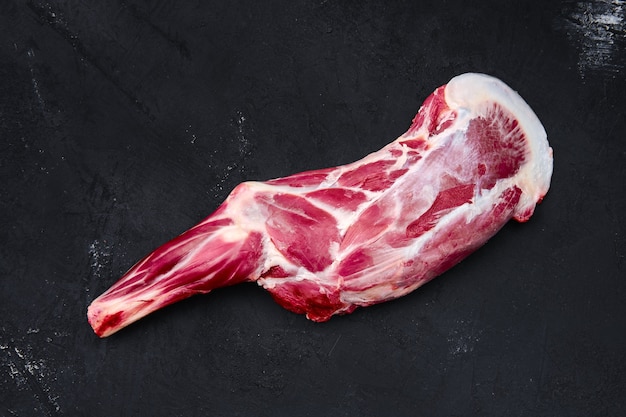 Osso di coscia di agnello crudo fresco sul tagliere di legno con erbe e condimento