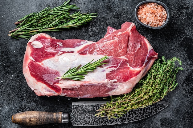 Fresh Raw lamb mutton shoulder meat with butcher knife. Black background. Top view.