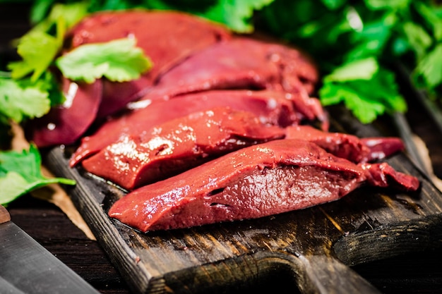 Fresh raw liver on a cutting board with parsley and a knife