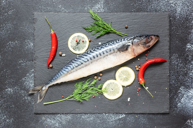 Fresh raw mackerel with spices and vegetables on black stone board top view