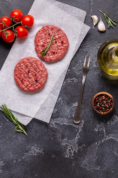 Cotoletta di hamburger di carne cruda fresca con erbe e spezie sulla tavola di pietra nera, vista dall'alto