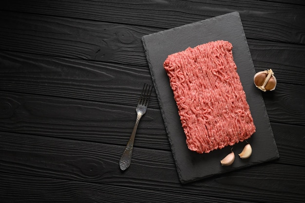 Fresh raw meat or ground chicken meat on a wooden cutting board with thyme spices and garlic Black wooden background Top view Copy space