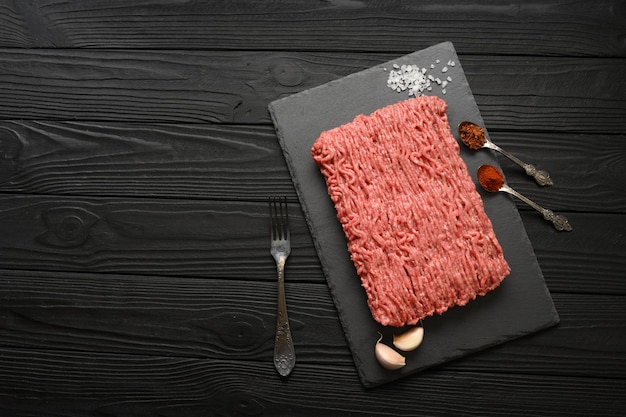 Fresh raw meat or ground chicken meat on a wooden cutting board with thyme spices and garlic Black wooden background Top view Copy space