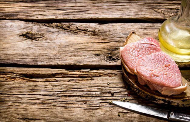 Fresh raw meat with knife and oil on a wooden stand on a wooden table