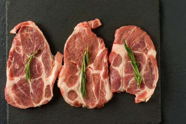 Свежее сырое мясо со специями и розмарином и красным перцем на черном сланце, на темном фоне, свинина, говядина, вырезка из костей.
