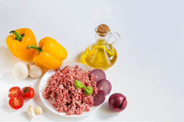 Fresh raw minced beef in a white plate with pepper, onion and tomatoes