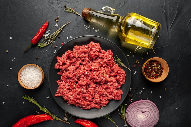 Fresh raw minced beef with herbs and spices on a black plate on a stone background