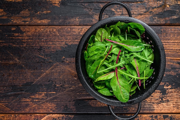 Fresh raw mixed greens, spinach, swiss chard and arugula. Dark wooden background. Top view. Copy space.