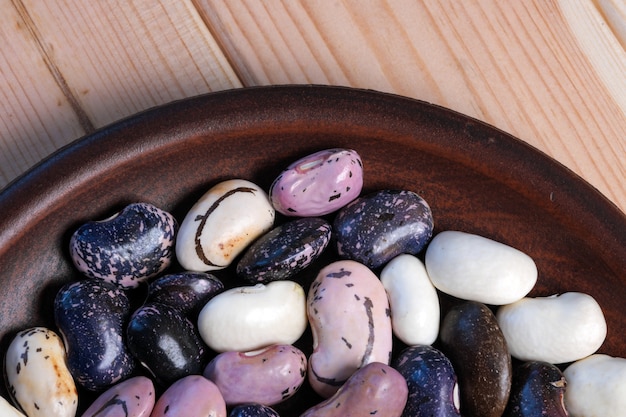 Fresh raw multicolored beans in a clay plate on a brown wooden background close-up