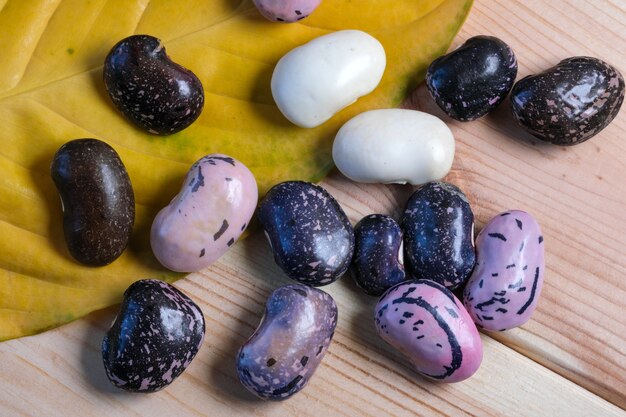 fresh raw multicolored beans in a clay plate on a brown wooden background close-up