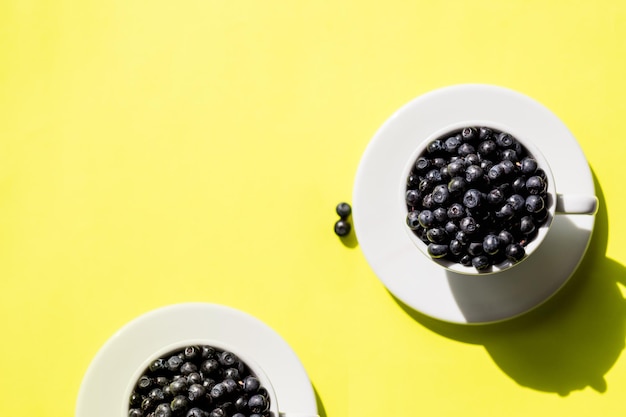 Fresh raw organic farm blueberry in white cup on yellow kitchen background copy spaceSummer seasonal natural vitamines and antioxidants Healthy diet and nutrition conceptflat lay