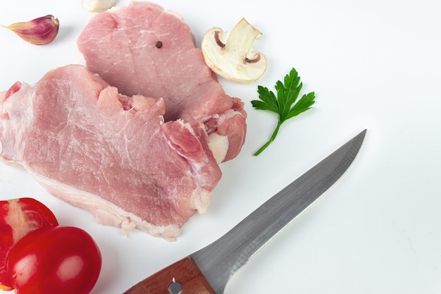 Fresh raw organic slice of braising steak fillet with meat hatchets garlic tomato spice pepper champignon on white background Salt and Pepper