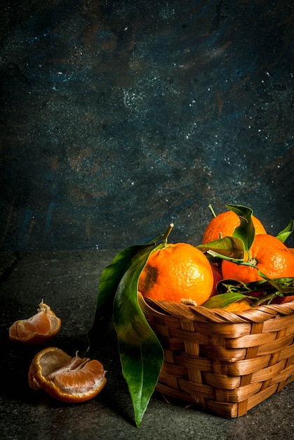 Fresh raw organic Tangerines with green leaves in little basket on dark concrete stone background, copy space