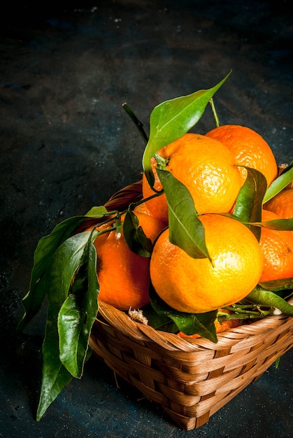 Fresh raw organic Tangerines with green leaves in little basket on dark concrete stone , 