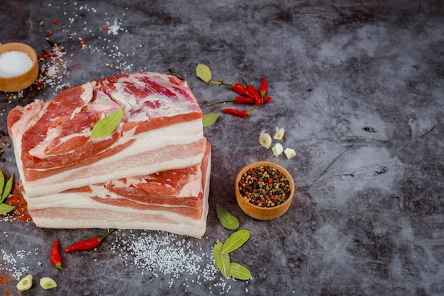 Fresh raw pork belly pieces on dark background with spices and herbs