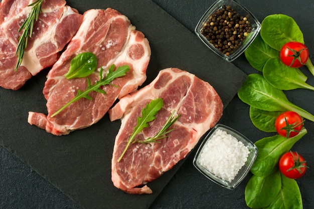 Photo fresh raw pork chop meat on a plack slate with rosemary and parsley and black pepper.