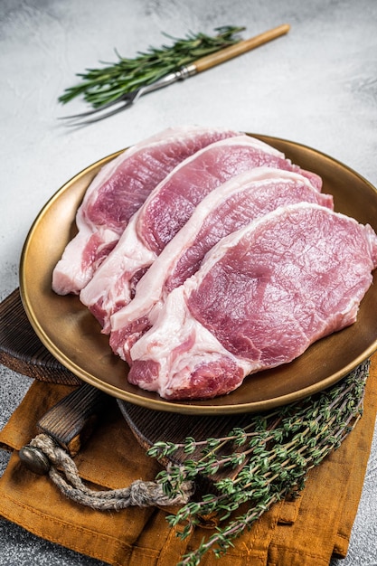 Fresh raw pork cutlet or chop steak on a plate with herbs White background Top view