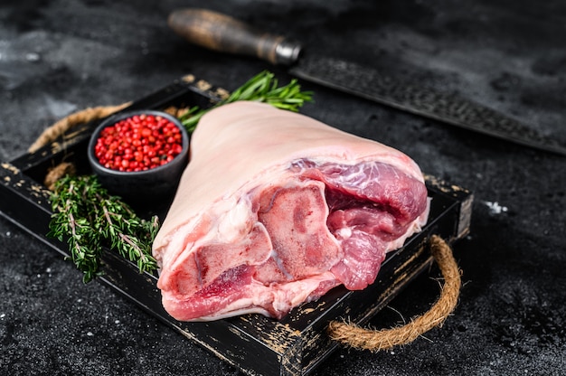 Fresh Raw pork Eisbein knuckle ham in a wooden tray with meat knife. Black Wooden background. Top view.