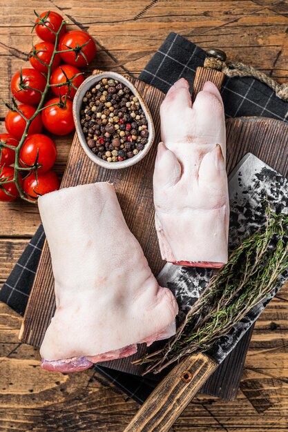 Fresh raw pork knuckle or hoof feet on a butcher board with\
cleaver wooden background top view