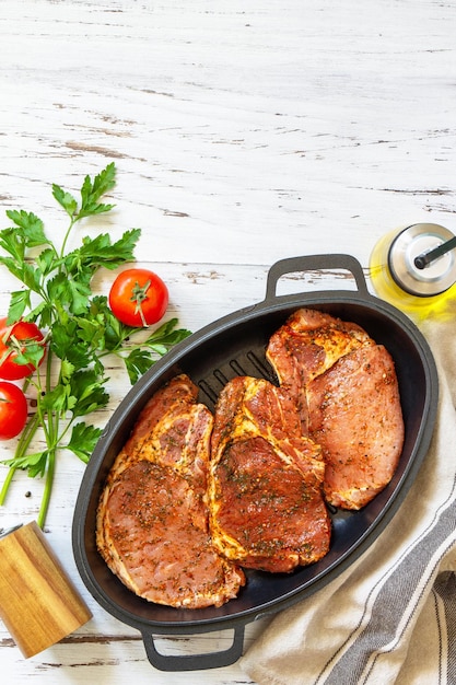 Fresh raw pork loin on the bone with spices and marinade in a cast iron pan on wooden table preparation for baking Top view flat lay Copy space