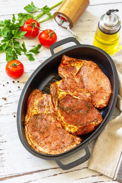 Fresh raw pork loin on the bone with spices and marinade in a cast iron pan on wooden table preparation for baking