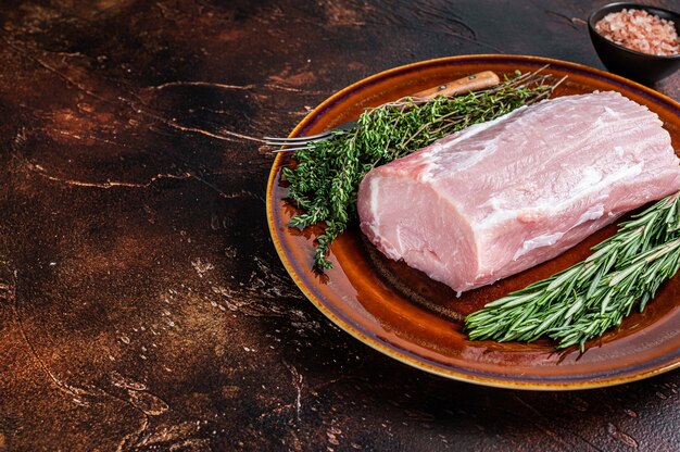 Fresh Raw pork loin meat with thyme and rosemary on rustic plate. Dark background. Top view. Copy space.