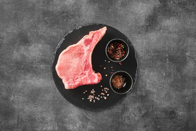 灰色の背景の上に塩とコショウで骨付き新鮮な生豚ロース肉