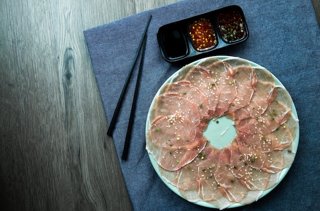 Fresh raw pork meat beef belly sliced on square dish disk plate on fabric and wood wooden background shabu hot pot ingredients