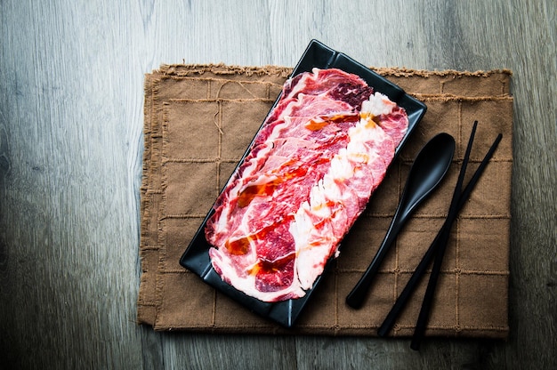 Fresh raw pork meat beef belly sliced on square plate on fabric\
and wood wooden background shabu hot pot ingredients