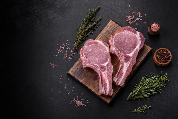 Fresh raw pork meat on the ribs with spices and herbs on a wooden cutting board on a dark concrete background