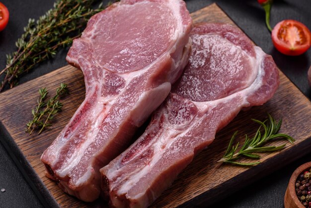 Fresh raw pork meat on the ribs with spices and herbs on a wooden cutting board on a dark concrete background