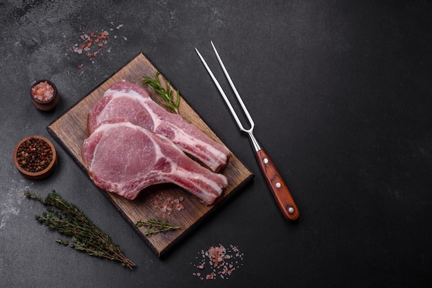 暗いコンクリートの背景に木製のまな板に香辛料とハーブを添えた肋骨に新鮮な生の豚肉