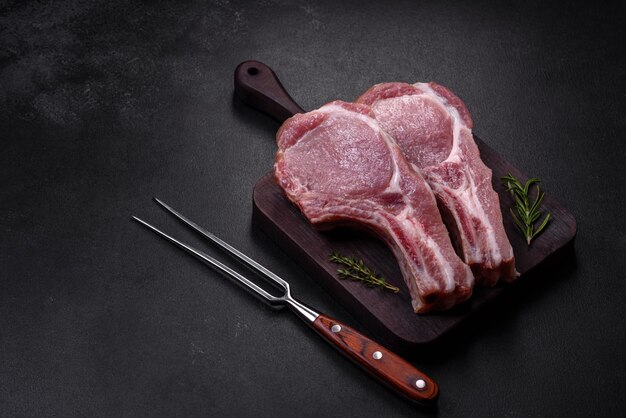 Fresh raw pork meat on the ribs with spices and herbs on a wooden cutting board on a dark concrete background