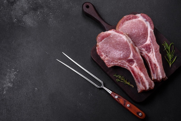 Fresh raw pork meat on the ribs with spices and herbs on a wooden cutting board on a dark concrete background