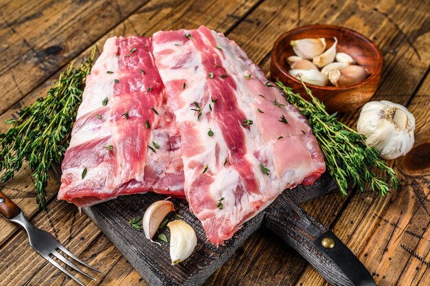 Fresh raw pork rack spareribs with thyme and garlic on cutting board. wooden background. Top view.