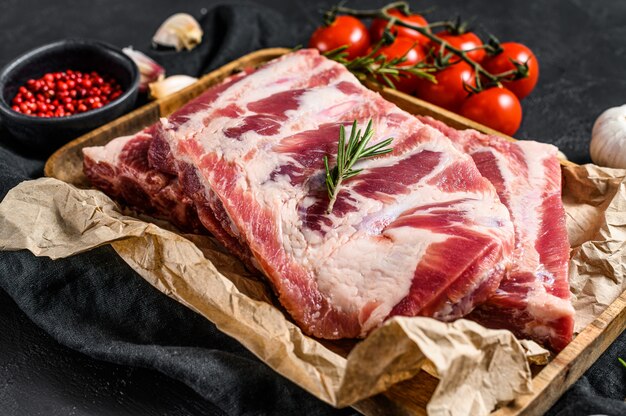 Costine di maiale crude fresche con rosmarino e aglio in una ciotola di legno.