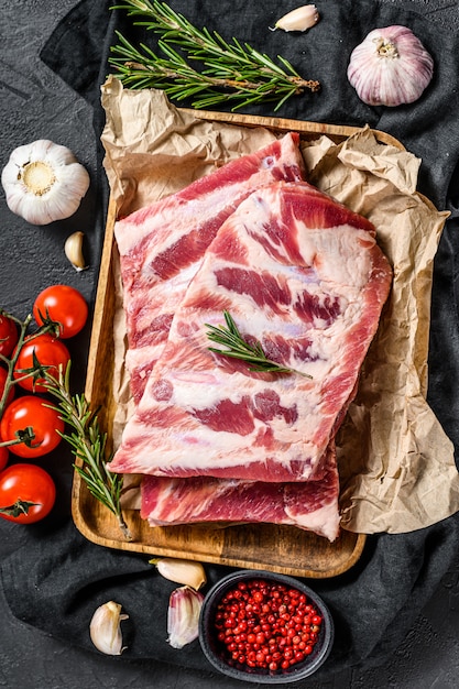 Costine di maiale crude fresche con rosmarino, pepe e aglio. fattoria biologica di carne. muro nero. vista dall'alto